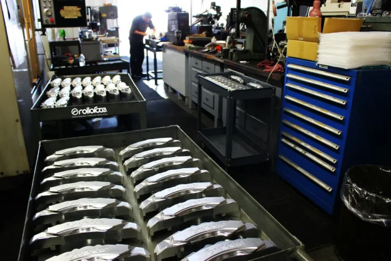 nside a machine shop with metal parts on carts in the foreground and a technician working at a bench in the background.